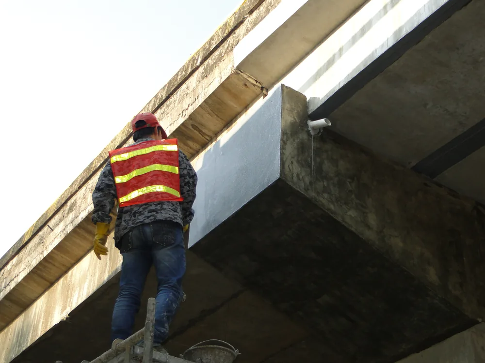 Worker applying BW6-9528 repair coating under bridge structure