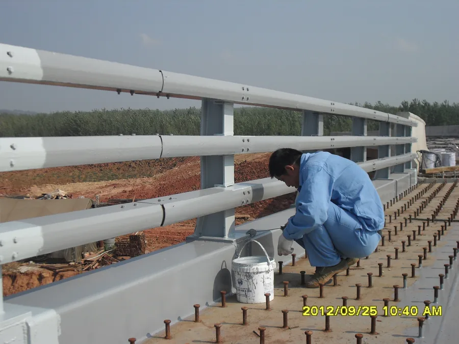 Worker applying protective coating around bridge railing base details
